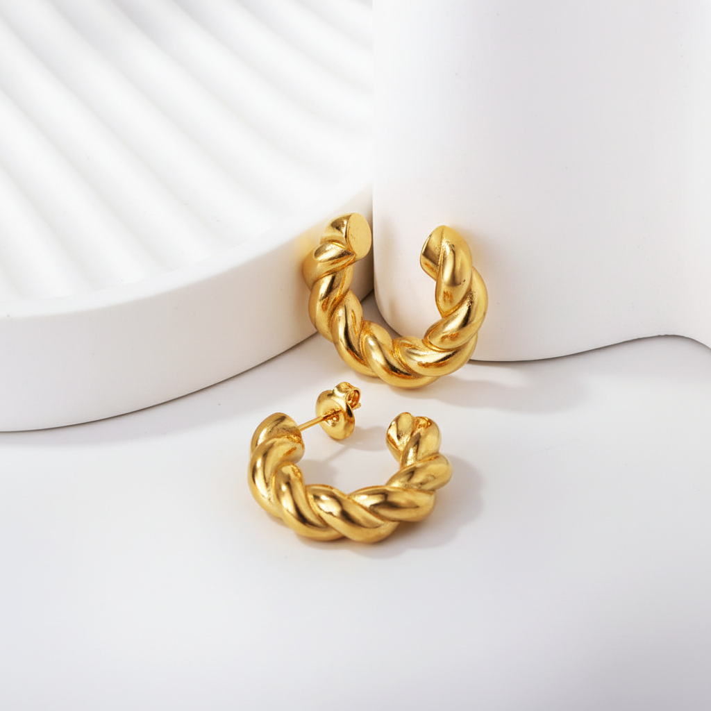 Chunky twisted rope gold hoop earrings on white ribbed ceramic tray